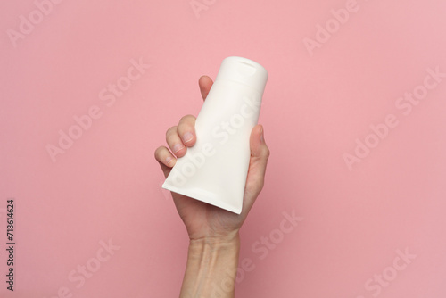 Female hand holding a white cream tube on a pink background