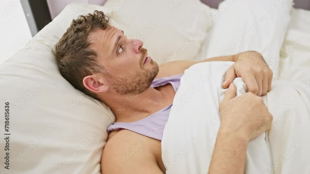 A concerned hispanic man with a beard lying in bed at home, displaying a sense of anxiousness or discomfort. A concerned hispanic man with a beard lying in bed at home, displaying a sense of anxiousness or discomfort.