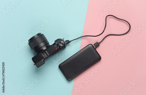 Modern mirrorless camera is charged from a power bank on pinbk blue background. Top view photo