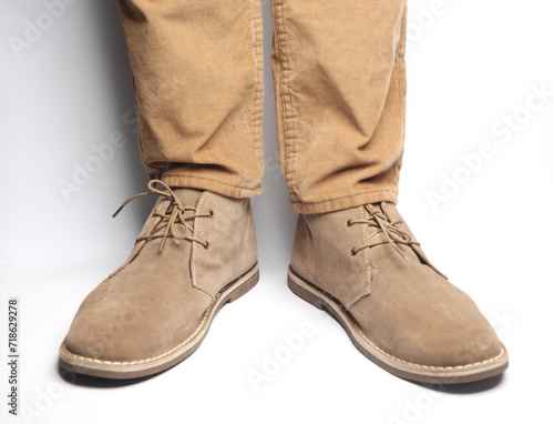 Male legs in beige pants and suede desert shoes on a white background
