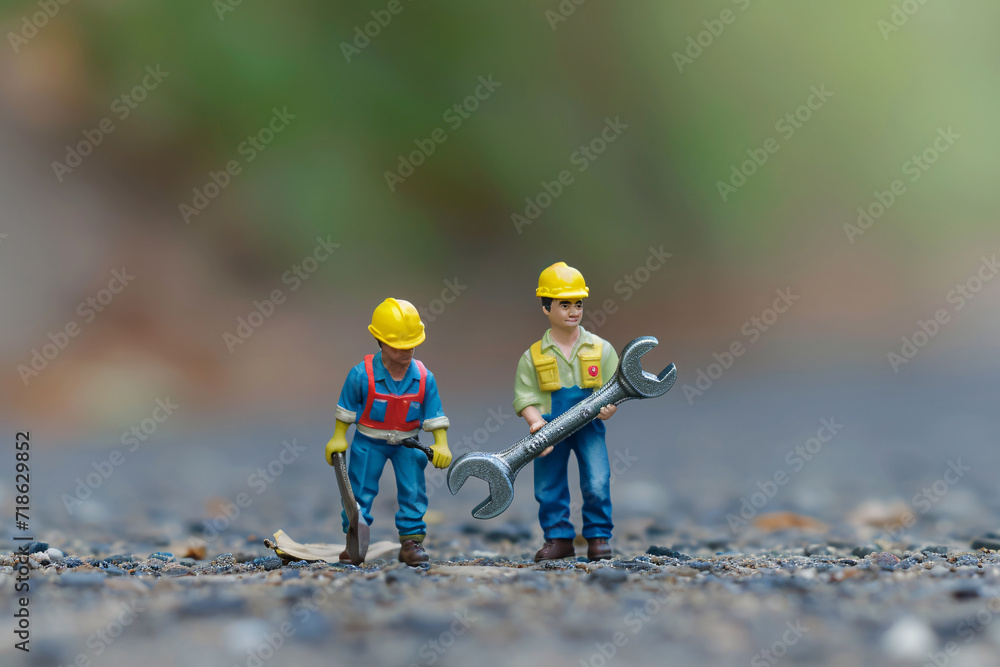 Fototapeta premium miniature workers carry a large wrench across a road