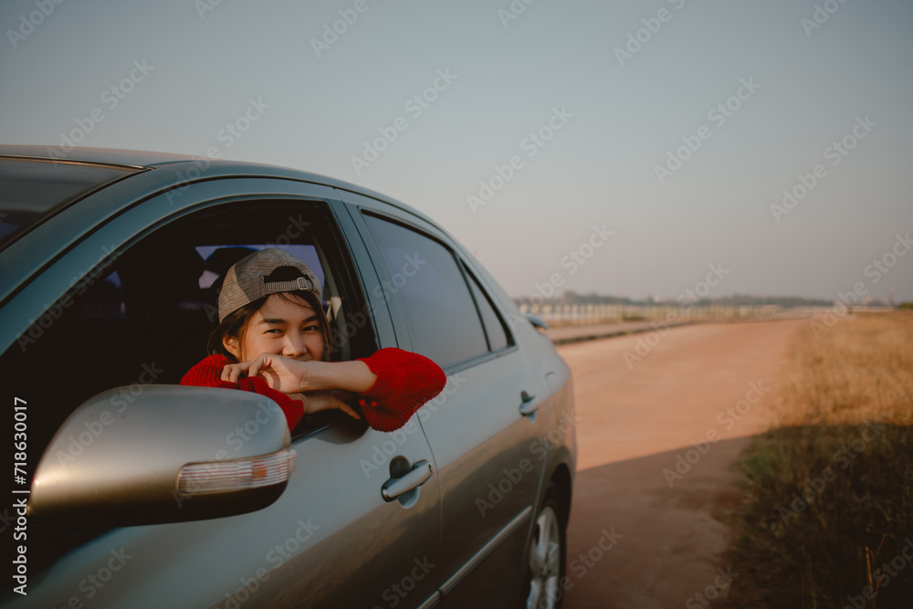Young Asian woman in red sweater leaning out of car window looking out to the field.