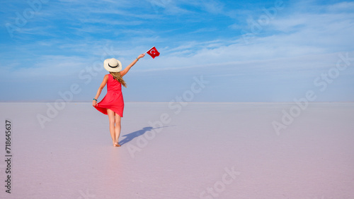 Young woman in red dress holding turkish flag and walking on salt lake, salt desert- Travel, tour tourism in Turkey