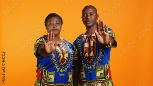 Confident ethnic couple showing stop sign in studio, raising palm and expressing their rejection. Man and woman doing refusal negative symbol, being displeased and disappointed.