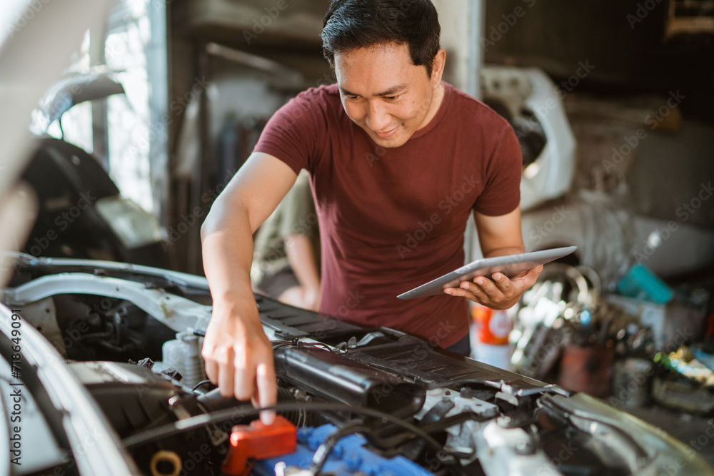 young male mechanic wiring a battery while using a digital tablet at a repair shop young male mechanic wiring a battery while using a digital tablet at a repair shop