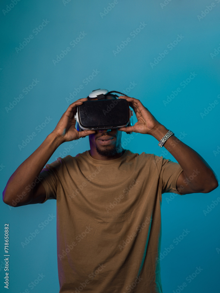 In a futuristic visual, an African American man stands isolated against a striking blue backdrop, adorned with VR glasses that transport him into a cutting-edge virtual reality experience, merging In a futuristic visual, an African American man stands isolated against a striking blue backdrop, adorned with VR glasses that transport him into a cutting-edge virtual reality experience, merging