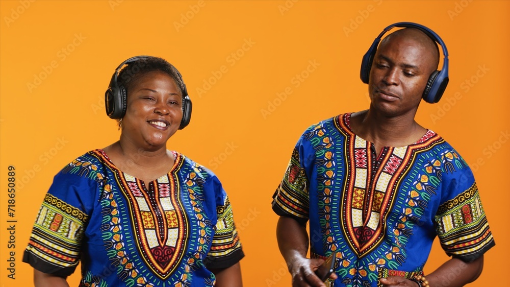 Obraz premium Joyful young couple enjoying music on headphones, dancing on camera on their wedding song and having fun. Ethnic married people feeling happy showing cool dance moves in studio.