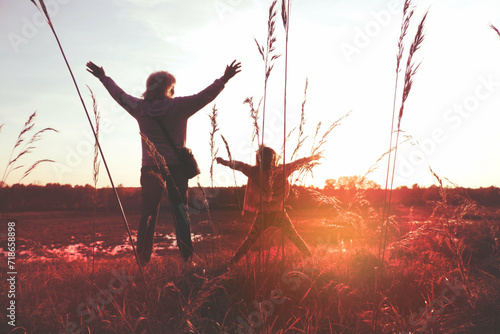 Child girl with mother in the meadow with raised hands, rear view. Relaxing. Summer sunset. Enjoying Life photo