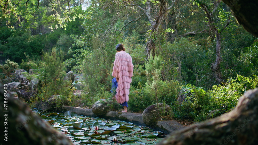 Magical woman walking forest lake wearing original dress. Girl looking on pond