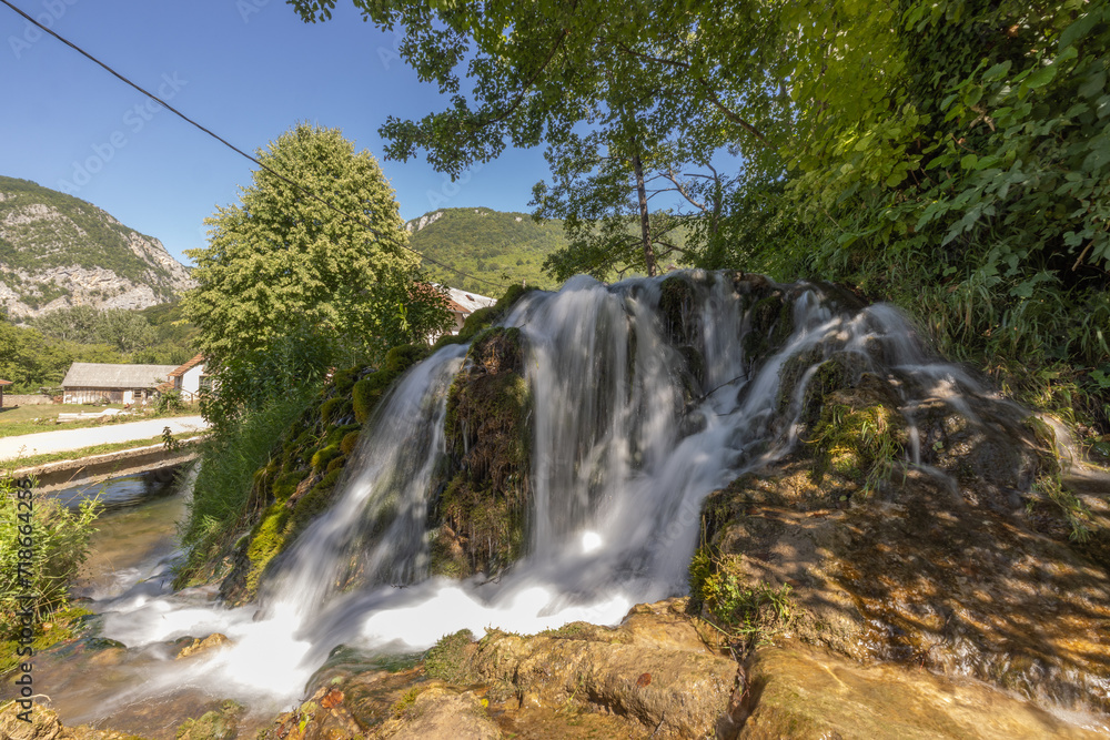 Fototapeta premium Small waterfalls on Una river, close to Martin Brod, Bosnia, on a summer day. Beautiful green river in a valley, with cascades and small waterfalls flowing.