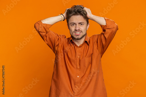 Sad young Caucasian man feeling hopelessness loneliness, nervous breakdown, loses becoming surprised by lottery results, bad fortune, loss unlucky news. Attractive guy isolated on orange background © Andrii Iemelianenko