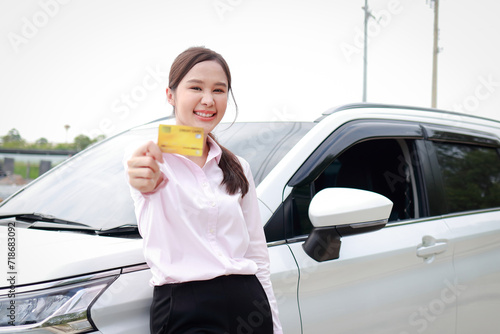 Beautiful smiling Asian woman standing in front of a car holding a credit card. Flexibility in spending. Financial concept. Insurance and car accidents