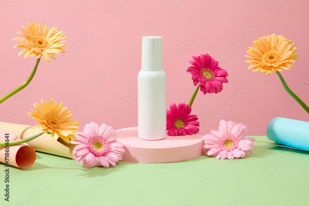 Front view of an unlabeled white cosmetic bottle displayed on a podium. The surrounding is decorated with bright gerbera flowers on a pastel background. Front view of an unlabeled white cosmetic bottle displayed on a podium. The surrounding is decorated with bright gerbera flowers on a pastel background.