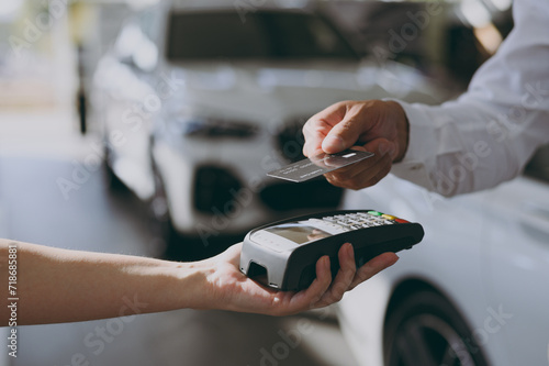 Close up cropped man customer male buyer client hold bank payment terminal process acquire credit card buy new auto automobile in car showroom vehicle salon dealership store motor show. Sales concept.