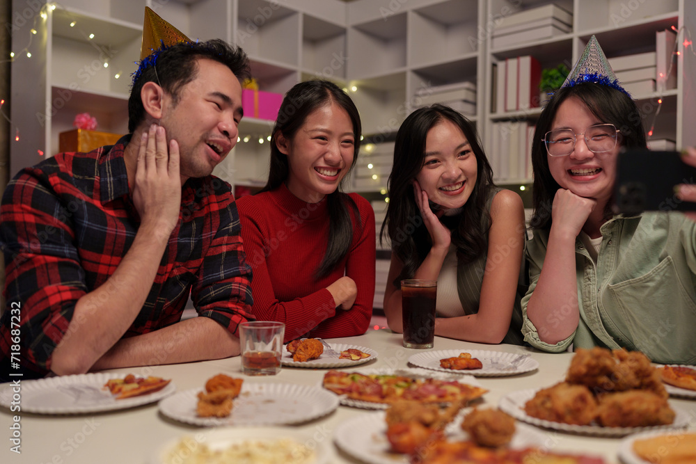 Group of cheerful Asian male and female friends having fun at a dinner party using cell phones to take selfies. Take photos together at home for a coworker reunion and celebrate the holiday season. Group of cheerful Asian male and female friends having fun at a dinner party using cell phones to take selfies. Take photos together at home for a coworker reunion and celebrate the holiday season.