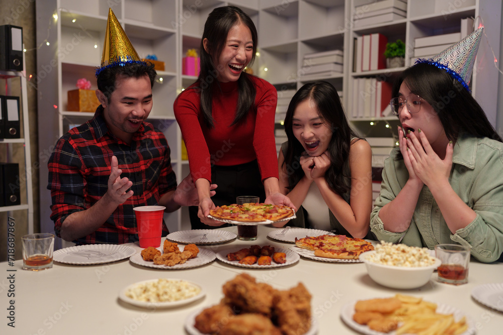 Group of happy young friends celebrating at a party with snacks popcorn pizza and drinks. The atmosphere at the event was full of laughter while sitting at the dining table together in the home office Group of happy young friends celebrating at a party with snacks popcorn pizza and drinks. The atmosphere at the event was full of laughter while sitting at the dining table together in the home office