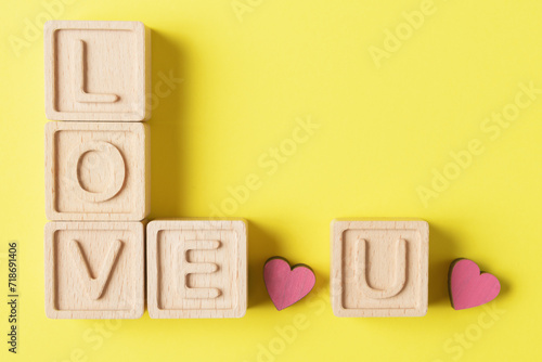 Wooden Blocks Spelling ‘LOVE U’ with pink Hearts on Yellow Background