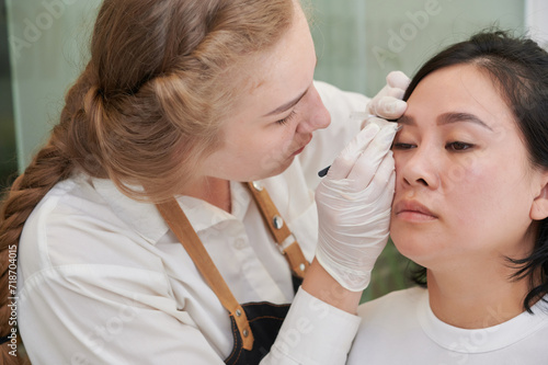 Young asian woman undergoing eyebrow correction procedure in beauty salon, closeup