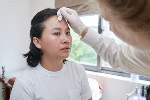 Young Asian woman undergoing eyebrow correction procedure in beauty salon, closeup