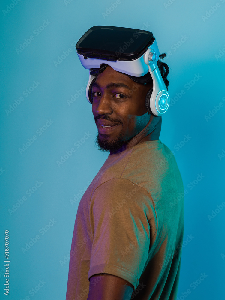 In a futuristic visual, an African American man stands isolated against a striking blue backdrop, adorned with VR glasses that transport him into a cutting-edge virtual reality experience, merging In a futuristic visual, an African American man stands isolated against a striking blue backdrop, adorned with VR glasses that transport him into a cutting-edge virtual reality experience, merging
