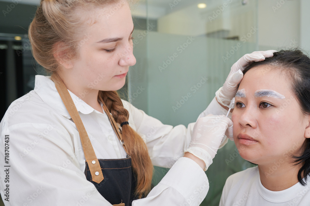 Fototapeta premium Young Asian woman undergoing eyebrow correction procedure in beauty salon, closeup