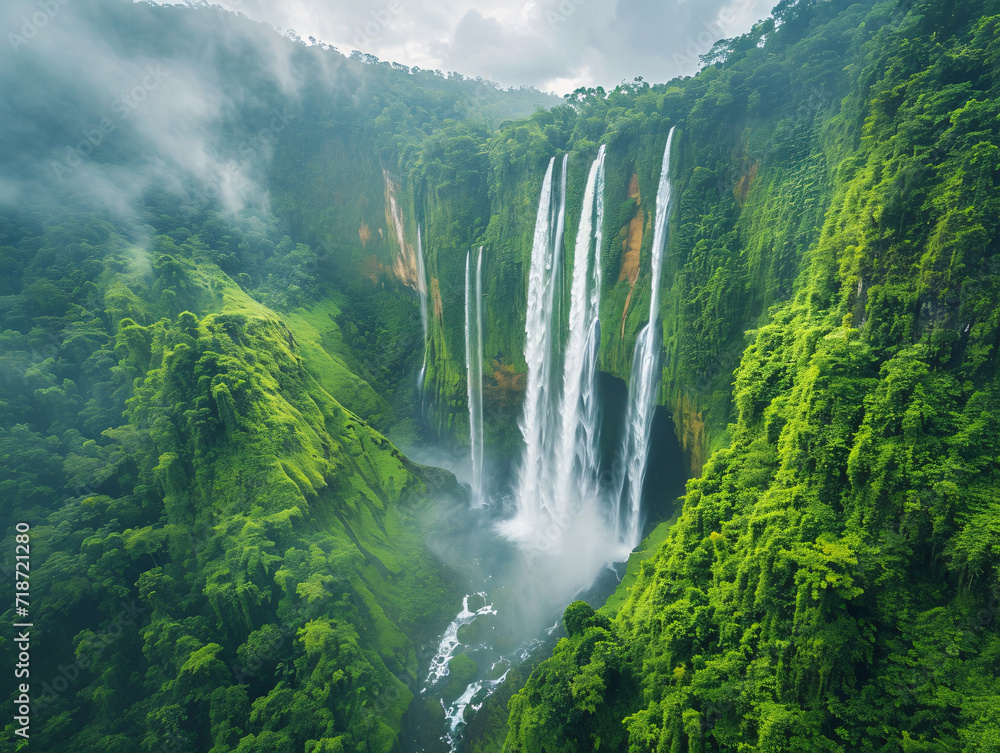 Aerial view of Tumpak Sewu Waterfalls cascading through dense tropical greenery. Nature and travel concept. Design for poster, wallpaper, eco-tourism brochure. Aerial photography with copy space
