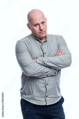Menacing bald man with crossed arms in a gray shirt. Aggression and intimidation. Isolated on a white background. Vertical. © Анна Демидова
