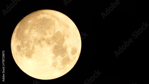 A glowing golden huge full moon seen from earth through the atmosphere against a starry night sky. A large full moon moves across the sky, the moon moving from the left frame to the right. photo