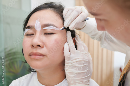 Fototapeta Naklejka Na Ścianę i Meble -  Young asian woman undergoing eyebrow correction procedure in beauty salon, closeup