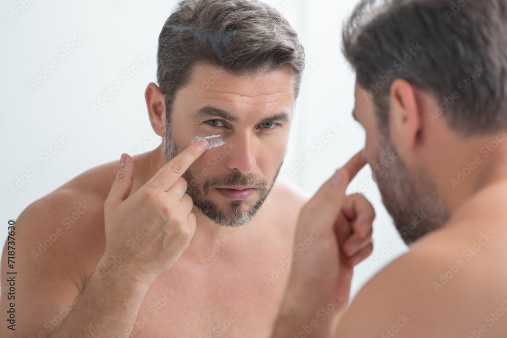 Fototapeta premium Sexy sensual man with perfect skin touch face after shaving. Skin care healthcare cosmetic procedures concept. Close up man looking in mirror, sensitive skin, cosmetology treatment. Skin care.
