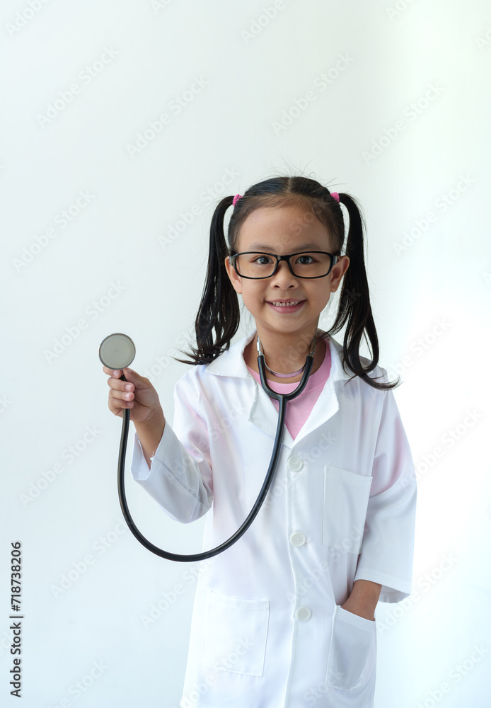 Girl wearing doctor's uniform and glasses standing smiling playing doctor, holding a stethoscope, showing gestures of treating a patient on a white background. future career concept. Girl wearing doctor's uniform and glasses standing smiling playing doctor, holding a stethoscope, showing gestures of treating a patient on a white background. future career concept.