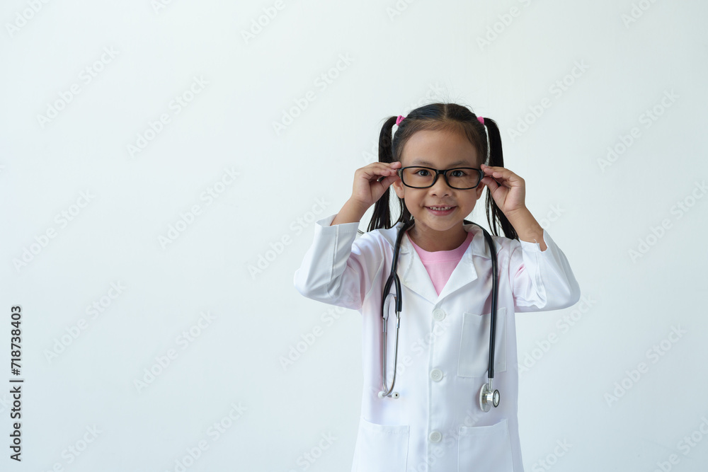 A young girl wearing a doctor's uniform and wearing glasses stands smiling and holds glasses playing doctor, showing gestures, emotions, thoughts, interest in this profession on a white background. A young girl wearing a doctor's uniform and wearing glasses stands smiling and holds glasses playing doctor, showing gestures, emotions, thoughts, interest in this profession on a white background.