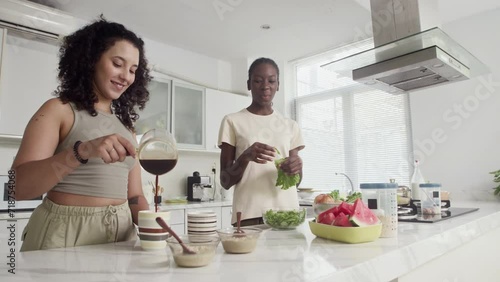 Low angle of cheerful female roommates drinking coffee and cooking healthy breakfast at kitchen photo