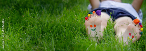 Children's legs with a pattern made of paints are smiling on the green grass