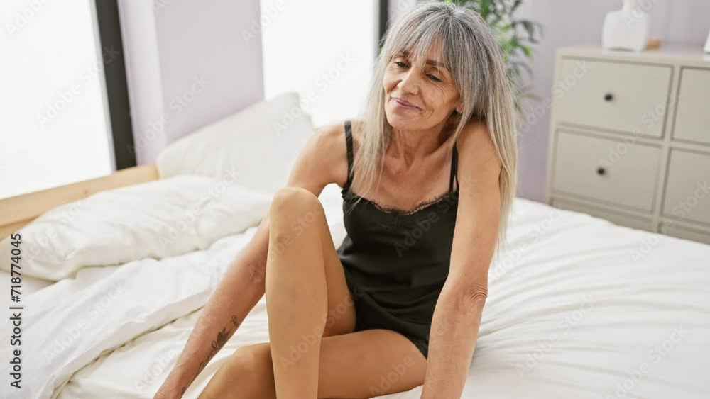 Mature hispanic woman with grey hair sitting in bedroom, looking contemplative and relaxed. Mature hispanic woman with grey hair sitting in bedroom, looking contemplative and relaxed.