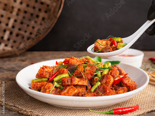 Use spoon to pick up stir fried crispy pork with red curry in white plate on wooden table background. Thai Food