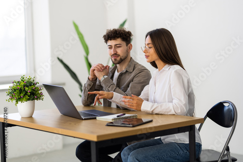 Two young businessmen and businesswomen sitting in the office, talking and surfing the internet together with a laptop