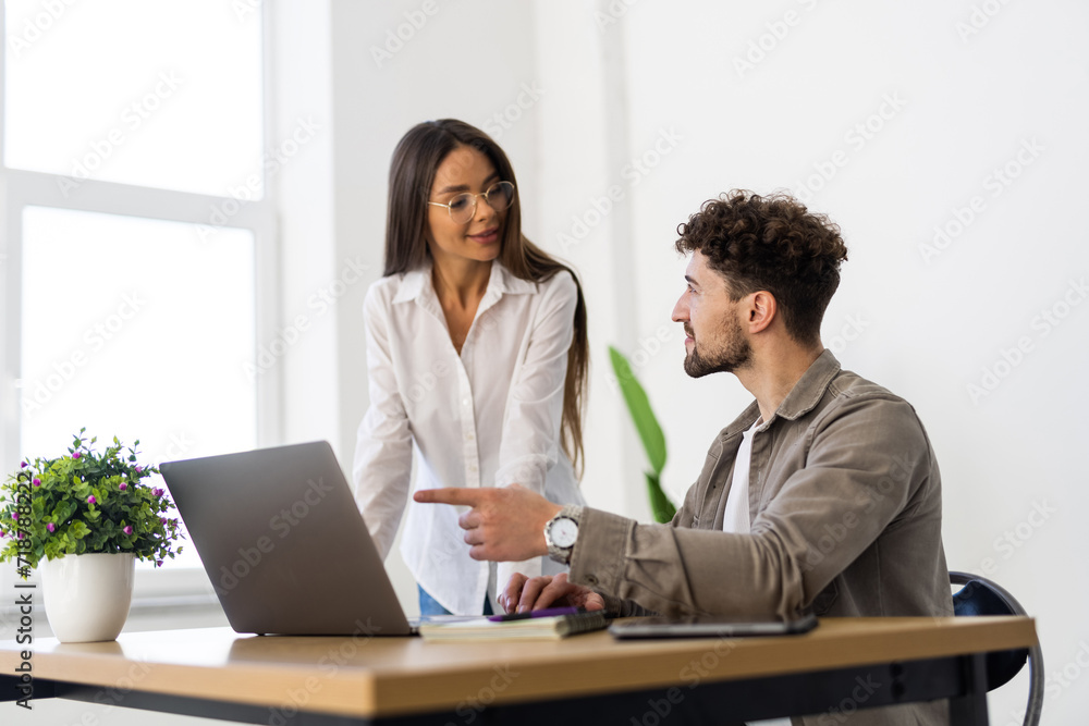 Professionals standing in an office and using a laptop together. Two young business people discussing a project. Professionals standing in an office and using a laptop together. Two young business people discussing a project.