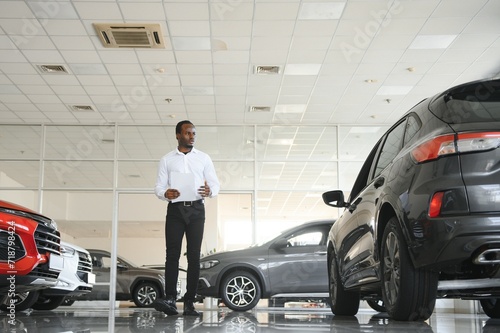 Portrait Of Handsome African American Salesman At Workplace In Car Showroom