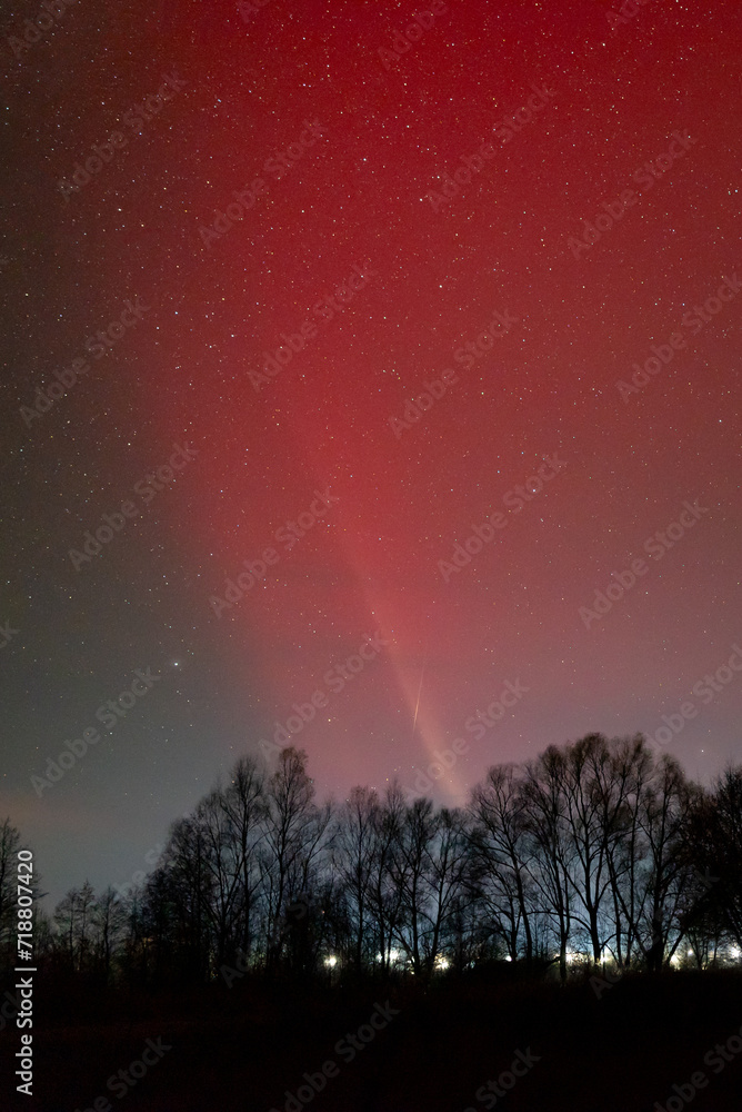 Bright red pillar of light in sky above some settlement. Aurora lights illuminating sky at night