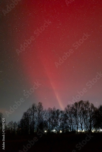 Bright red pillar of light in sky above some settlement. Aurora lights illuminating sky at night