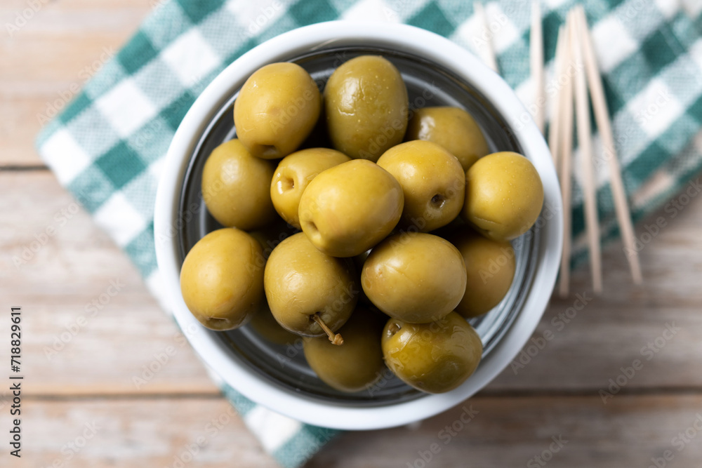Green olives in a bowl on wooden table. Top view
