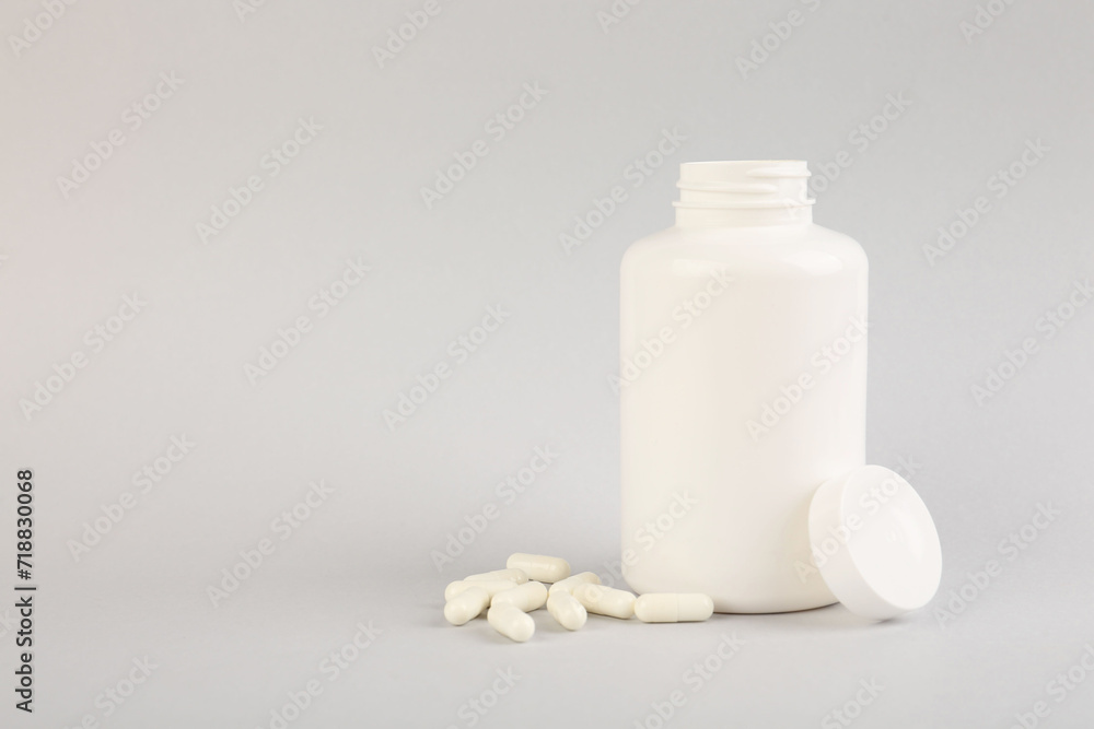 Blank white jar with vitamin capsules on light grey background, space for text Blank white jar with vitamin capsules on light grey background, space for text