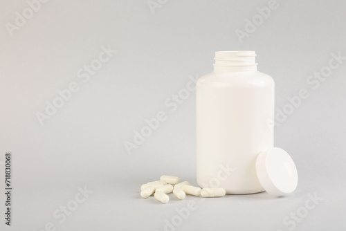 Blank white jar with vitamin capsules on light grey background, space for text