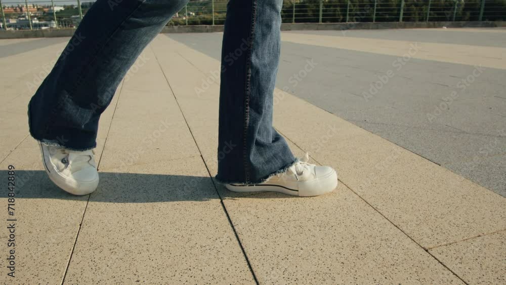 Young woman wearing blue jeans and white sneakers walking on asphalt road at sunny day close-up. Walk on pavement on the street outdoor. Young woman wearing blue jeans and white sneakers walking on asphalt road at sunny day close-up. Walk on pavement on the street outdoor.