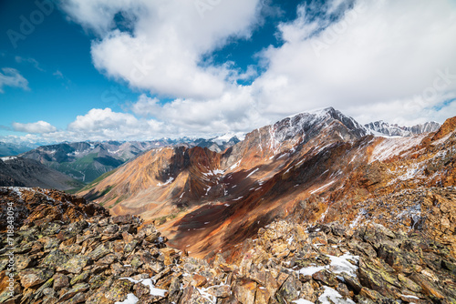 Scenic top view from stony precipice edge to multicolor big rocky ridge in freshly fallen snow and giant snow-capped mountain peak in low clouds. Snow-covered multi-color sharp rocks in huge mountains © Daniil