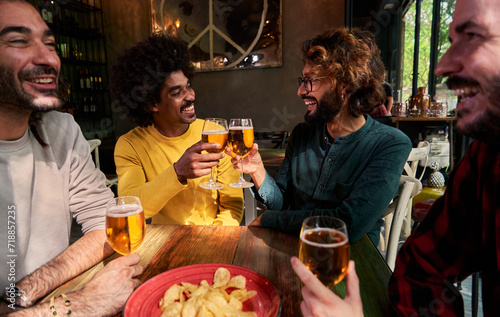 Multiethnic group of four male friends social gathering in a bar drinking beer and cheering celebrating together  having fun. Copy space.