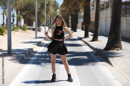 Blonde, young and beautiful woman dressed in black skirt and black top is passing through a pedestrian crossing. The woman crosses the street and takes the opportunity to do different poses.