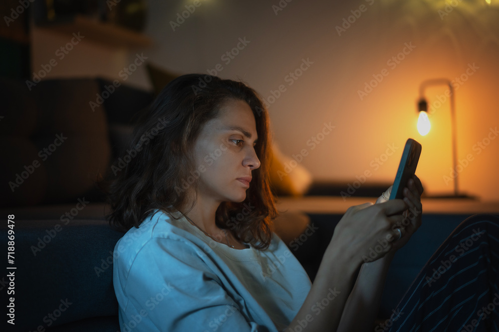 Young woman looking at smartphone screen while sitting at home in the evening