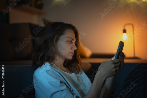 Obraz na płótnie Young woman looking at smartphone screen while sitting at home in the evening w salonie